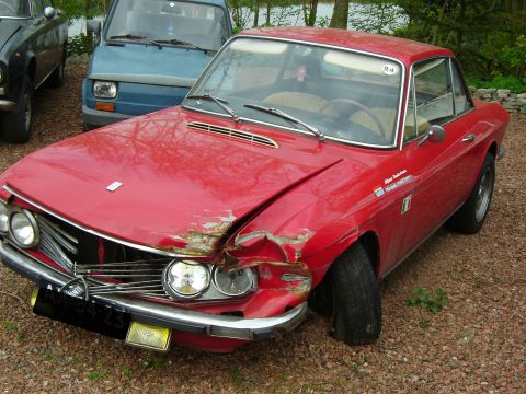 Een rode Lancia Flavia Coupé met voorschade, buiten.