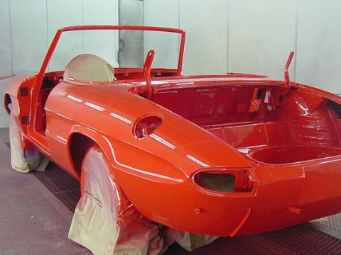 Een rood gespoten cabriolet-carrosserie in de spuitcabine.
