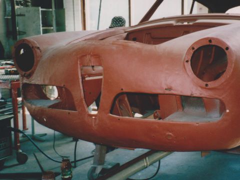 Een carrosserie in rode grondverf, met de koplampopeningen nog open.