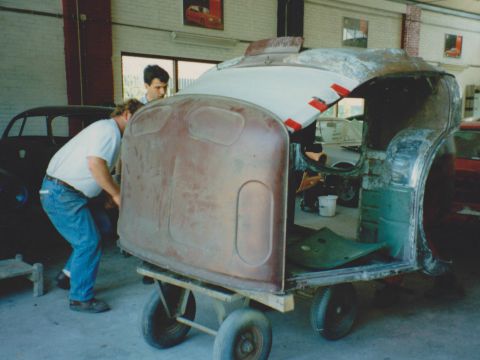 Een monteur bij een kale carrosserie op een transportwagen.